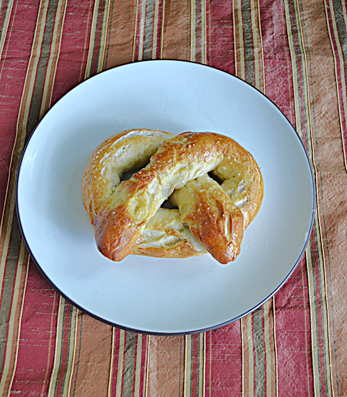 A plate with a golden brown soft pretzel on it.