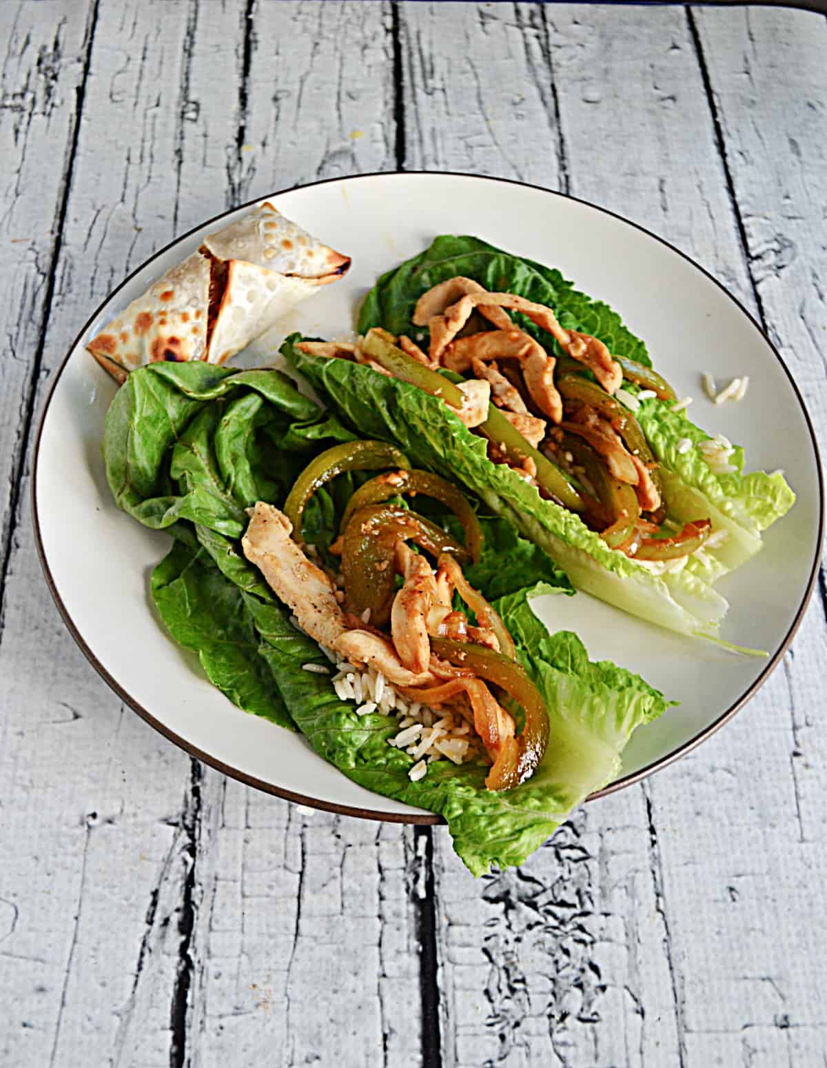 A plate with two lettuce wraps filled with chicken , peppers, and onions with an egg roll on the plate.
