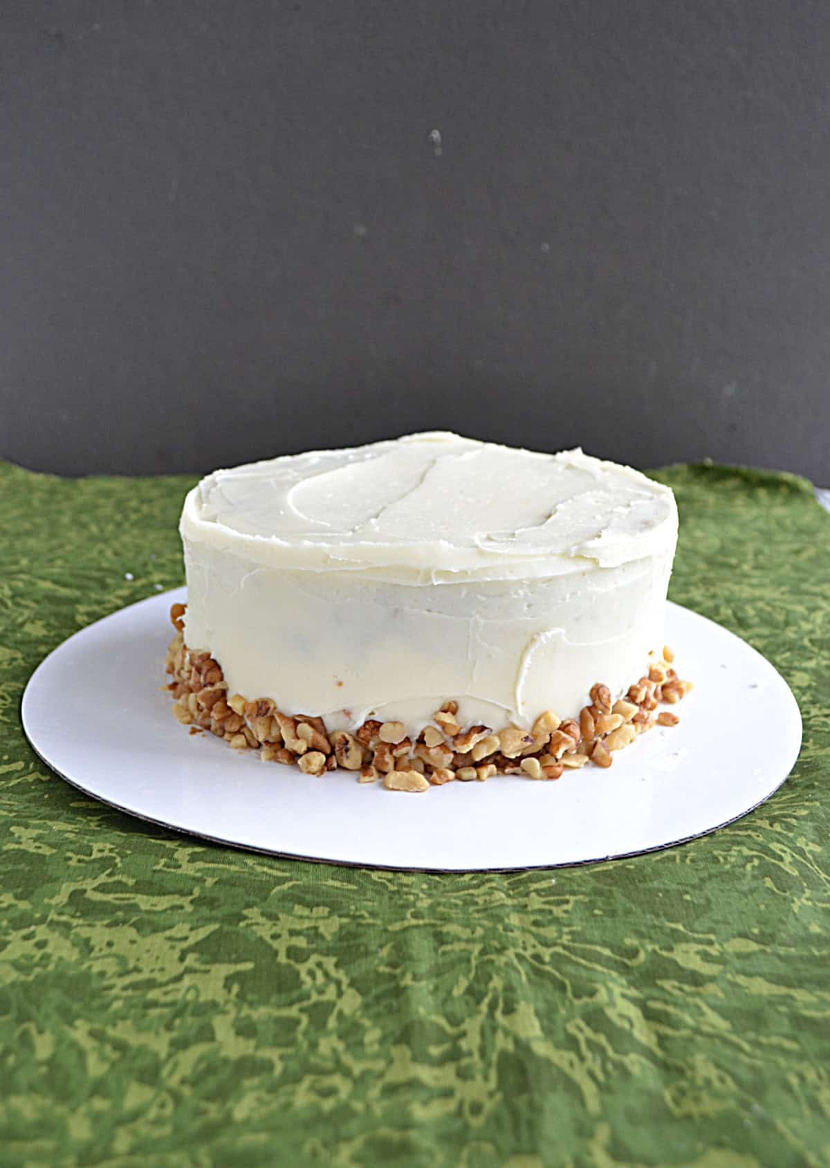 A cake with white frosting and nuts around the edges. 