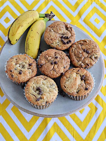 A plate of banana chocolate chip muffins with two mini bananas on the plate.