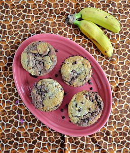 A pink platter topped with 4 banana chocolate chip muffins and two bananas on the side.