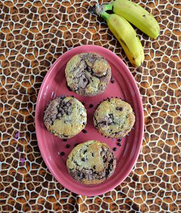 A pink oval platter topped with 4 banana chocolate chip muffins and two bananas on the side.