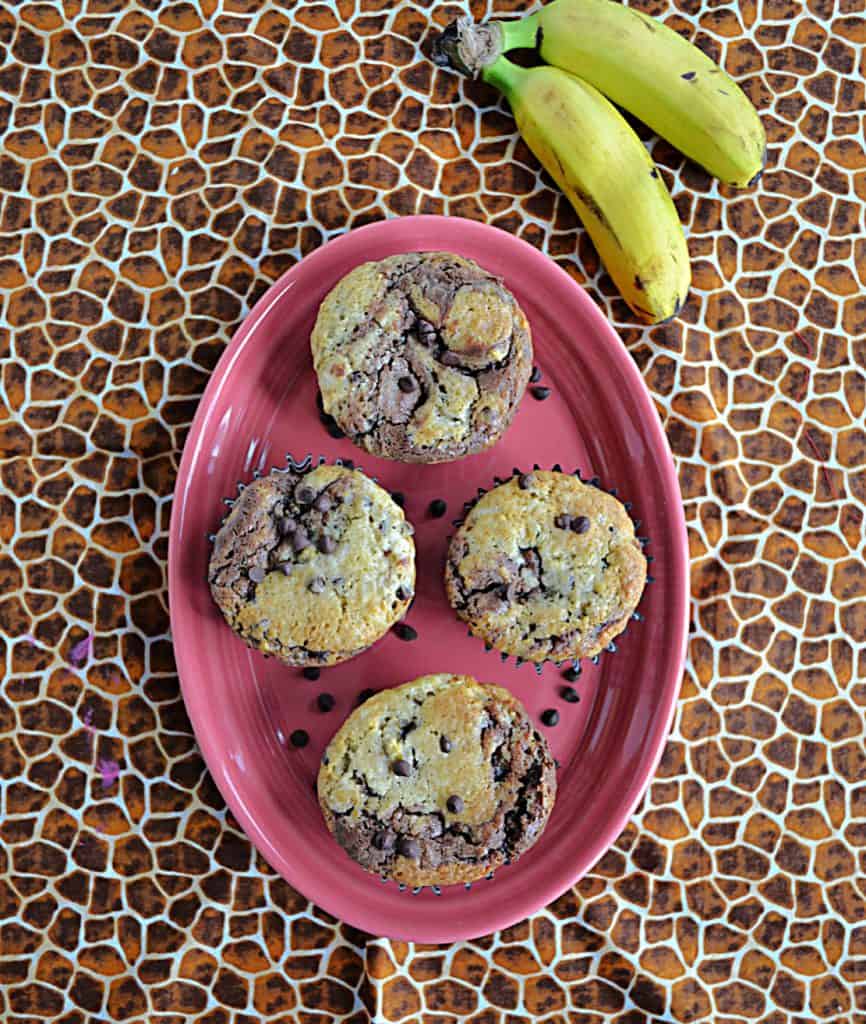 A pink oval platter topped with 4 banana chocolate chip muffins and two bananas on the side.