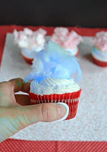 A close up of a cupcake with blue cotton candy on top.