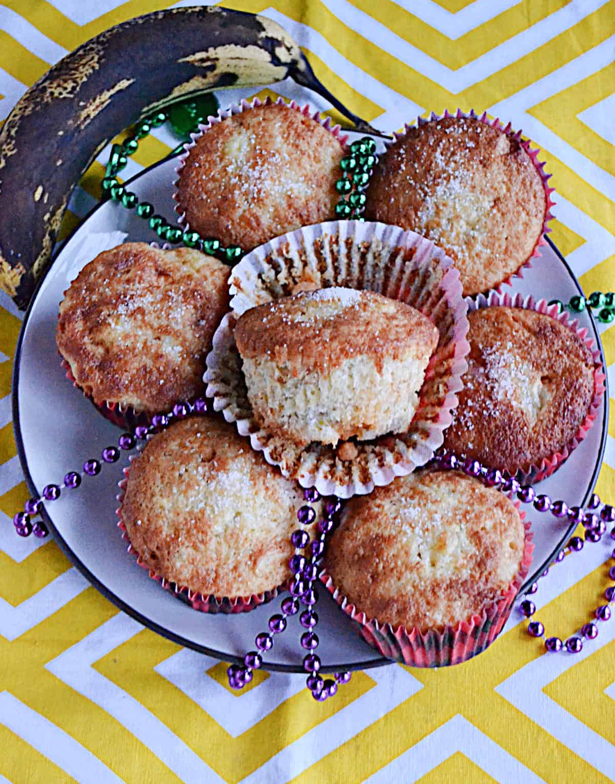 A plate of muffins with one muffin on top and out of the wrapper.