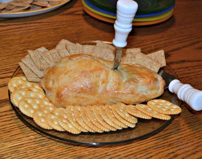 Brie baked in puff pastry with a cheese knife in it with crackers all around it. 