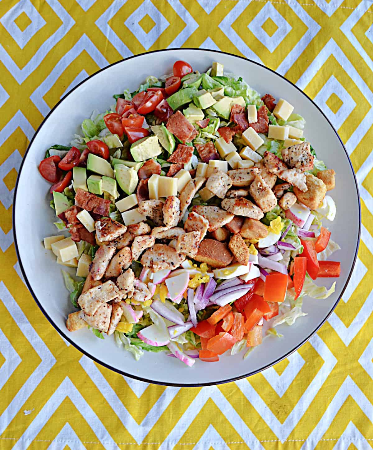 A plate of salad with chicken , bacon, avocado, cheese, peppers, tomatoes, and croutons on it.