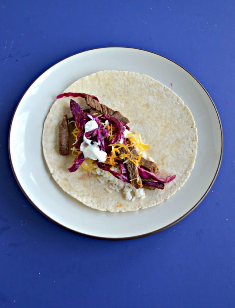 Blue background with a plate. On the plate is tortilla, beef, and pickled cabbage.