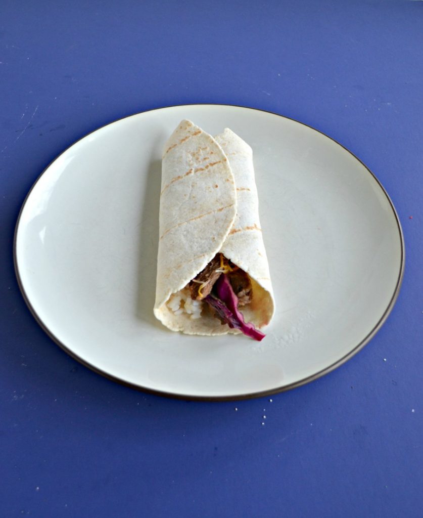 A Korean style beef taco rolled up in a tortilla on a plate with a blue background.