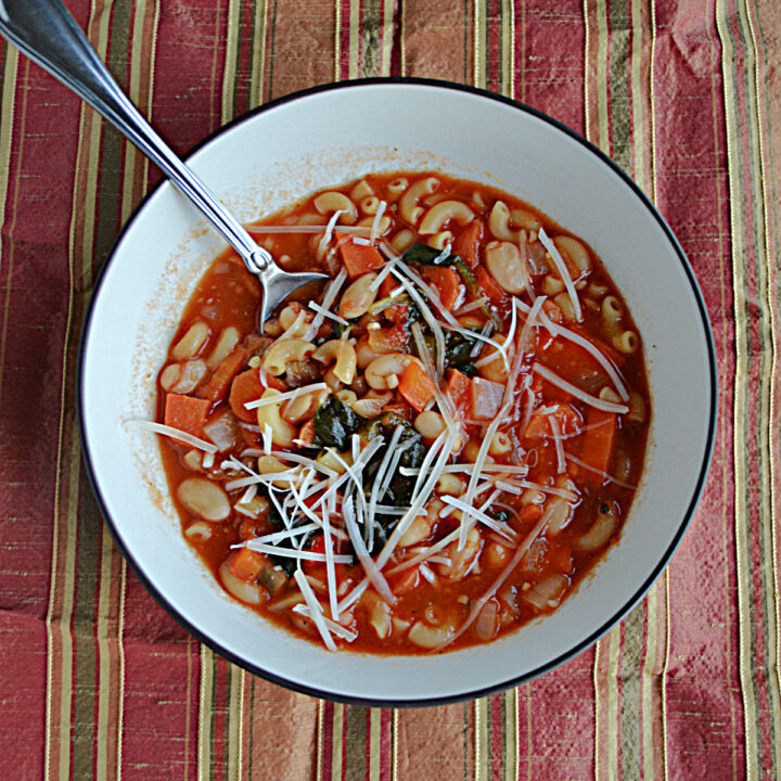 A bowl of Pasta e Fagioli with pasta and beans and Parmesan cheese with a spoon in it.