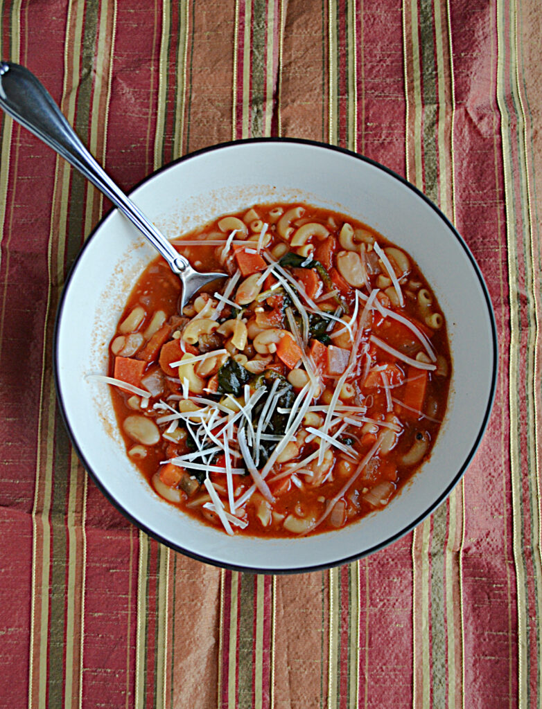 A bowl of Pasta e Fagioli with pasta and beans and Parmesan cheese with a spoon in it. 