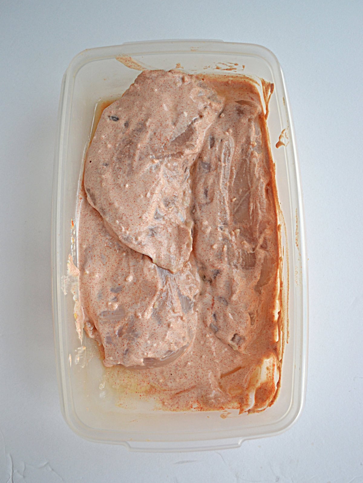 Chicken in a container of marinade.
