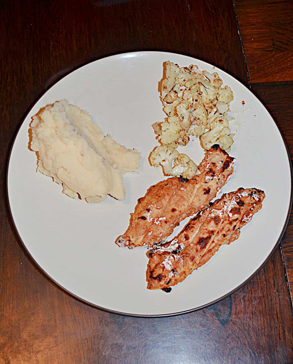 A plate with two pieces of chicken, a scoop of mashed potatoes, and a scoop of cauliflower.
