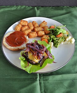 A plate with a burger, tater tots, and mixed vegetables on it.