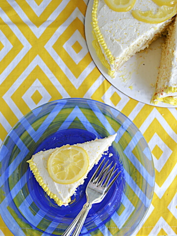 A slice of Lemonade Cake on a plate with two forks and the whole cake minus the piece on the plate.