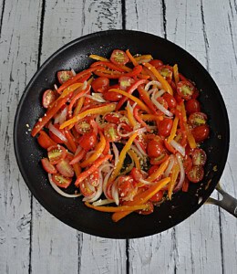 A skillet with peppers and onions and tomatoes in it.