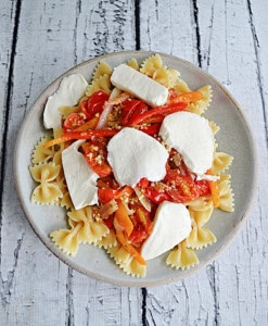 A plate of pasta with tomato and pepper sauce on top with slices of mozzarella on top.