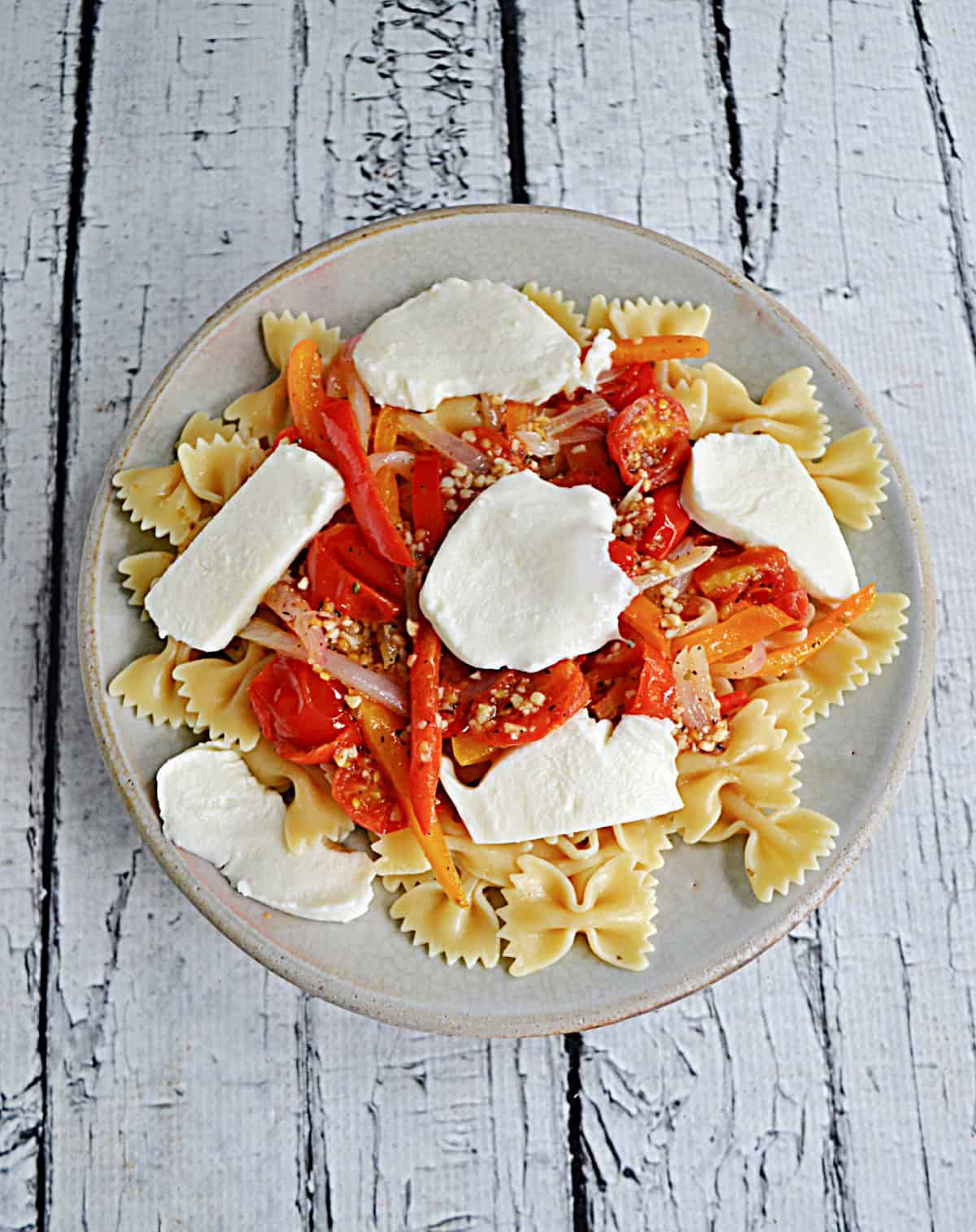 A plate of pasta with peppers and mozzarella slices on top.