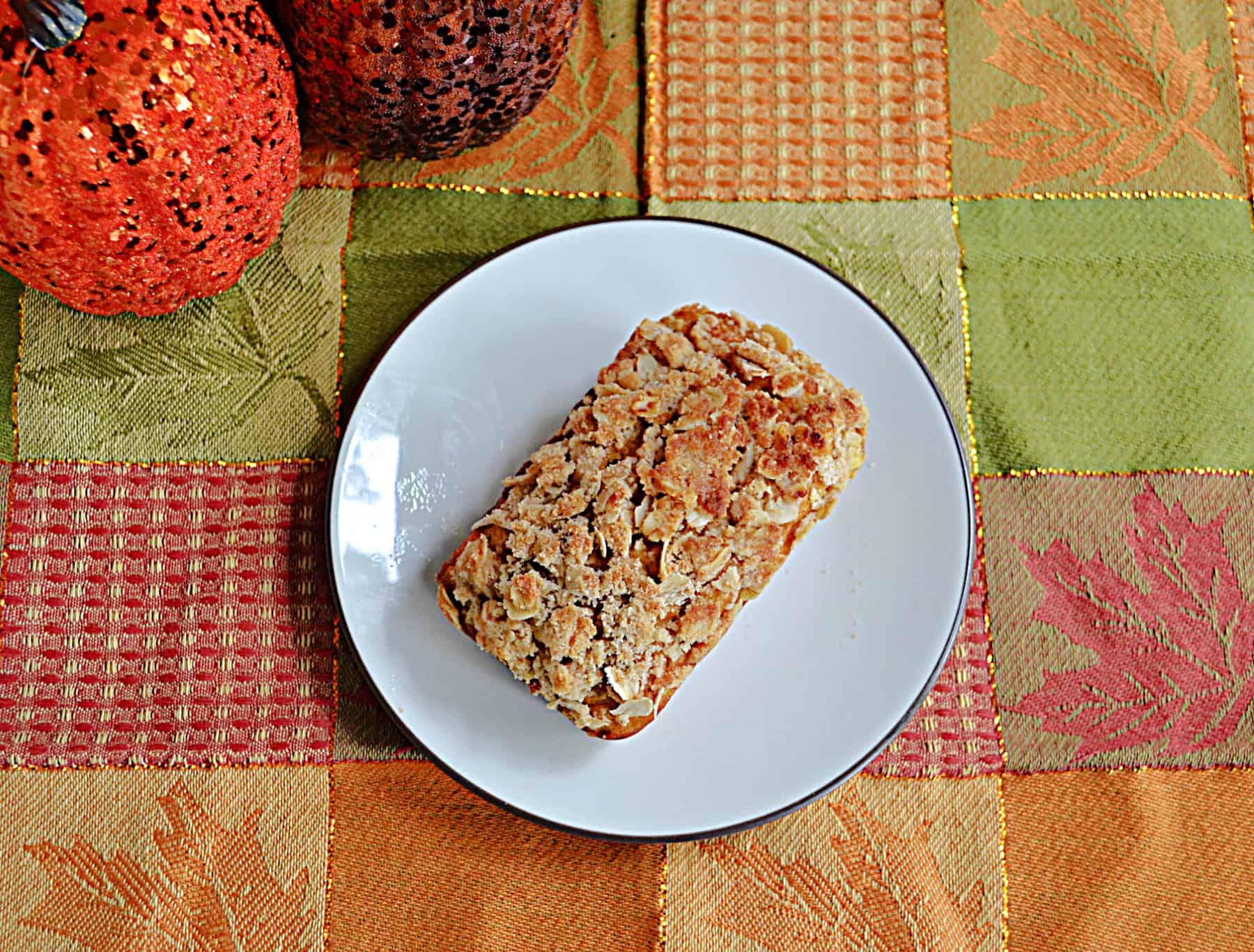 A plate with a mini bread loaf on it and pumpkins in the background.