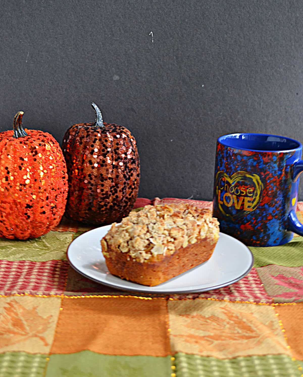 A plate with a mini loaf of bread on it with two pumpkins and a coffee cup behind it.