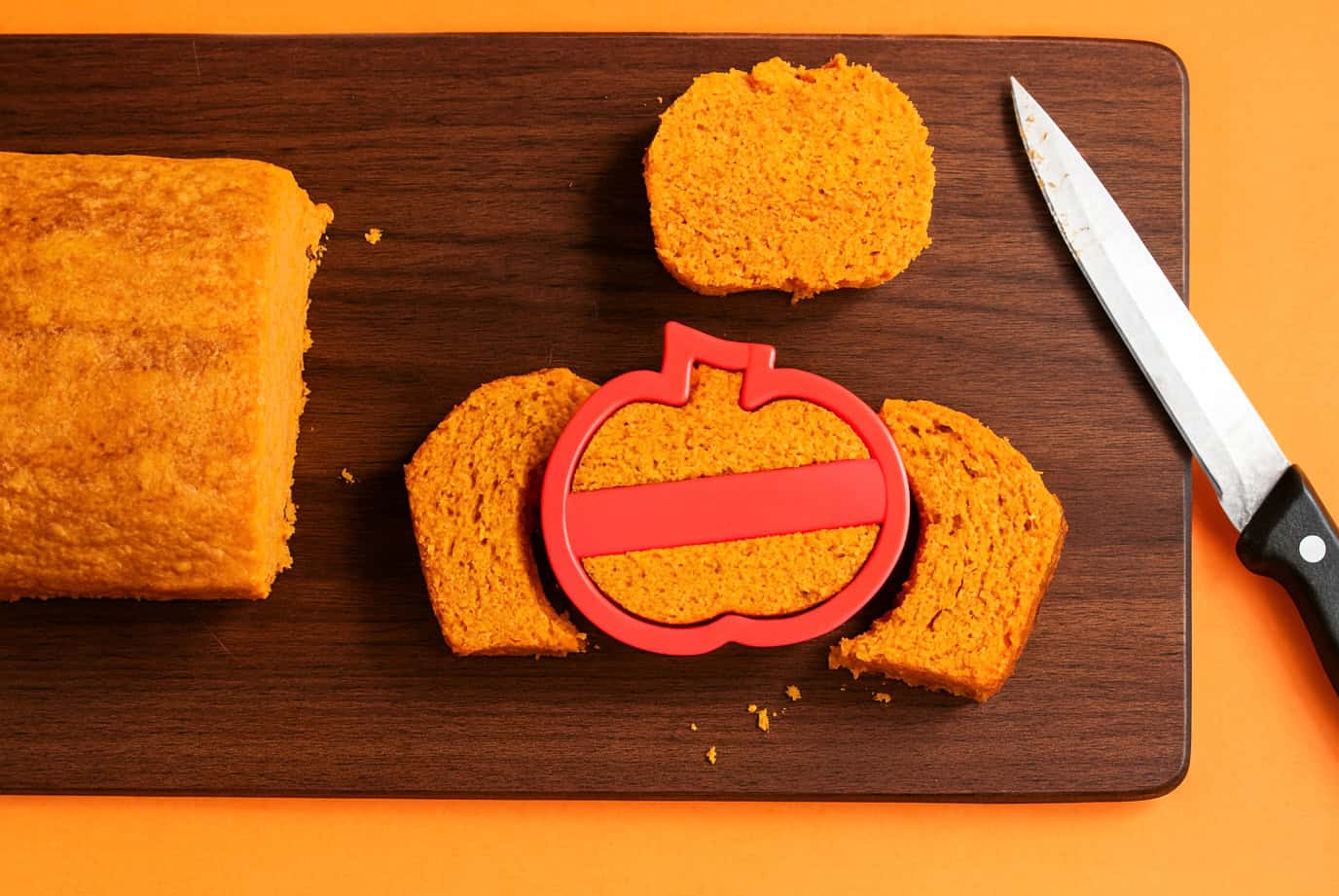 A cutting board with a pumpkin cookie cutter cutting out a slice of cake.