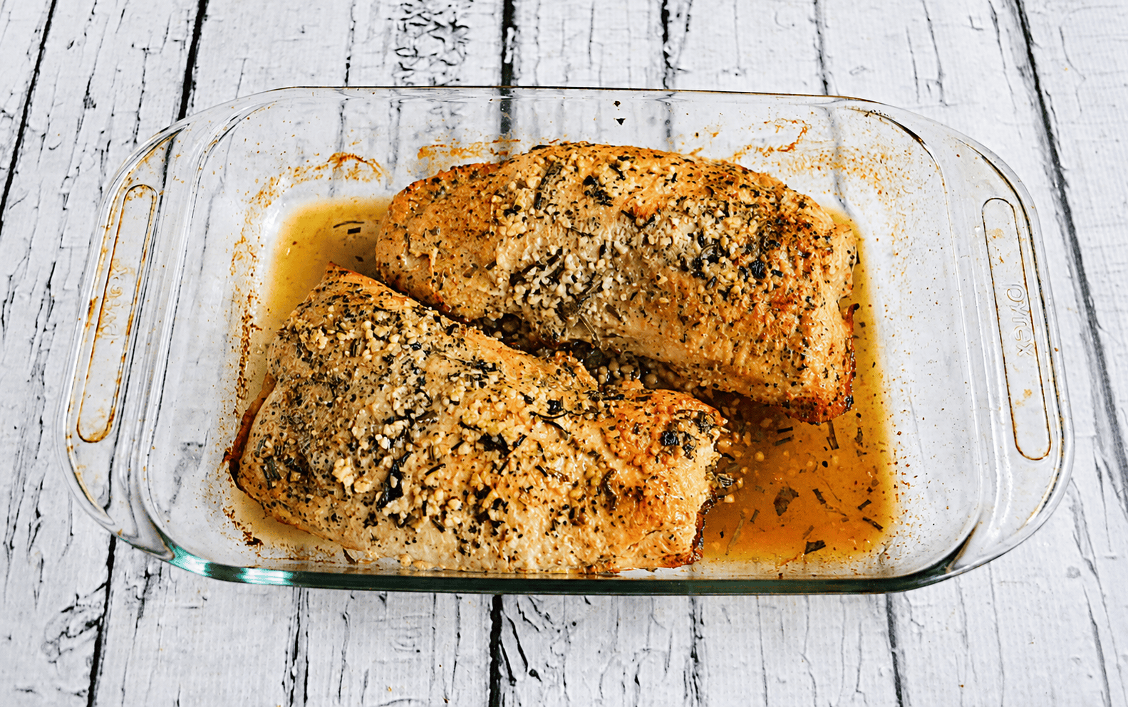 A baking dish with two turkey tenderloins topped with herbs, garlic, and butter.