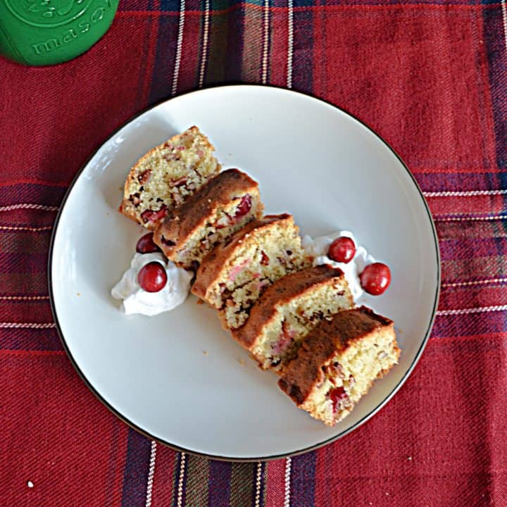 A top view of a plate with slices of cranberry pecan bread and dollops of whipped cream with cranberries on them.