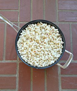A large, silver skillet full of fluffy white popcorn on top of a brick background.