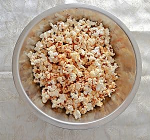 A silver bowl filled with popcorn sprinkled with red BBQ seasoning on a white background.
