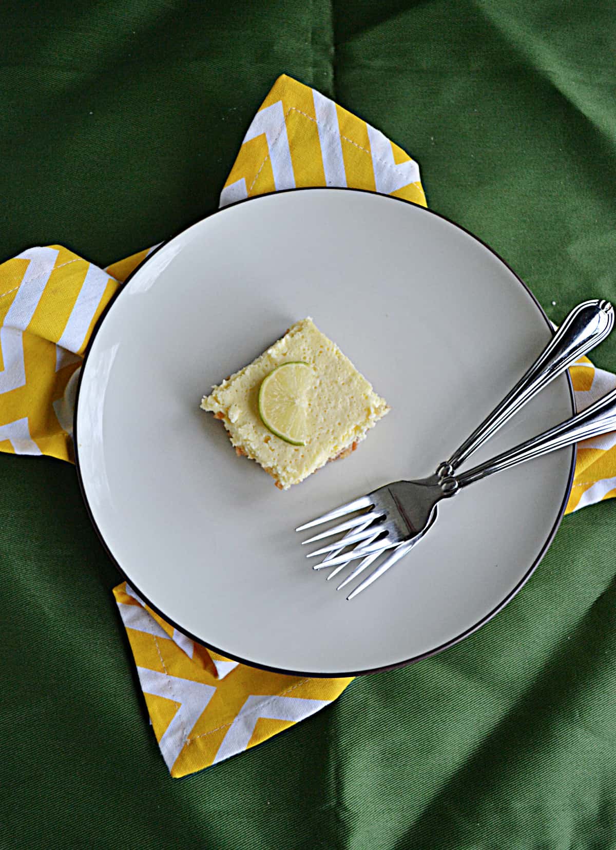 A plate with a margarita cheesecake bar with 2 forks.