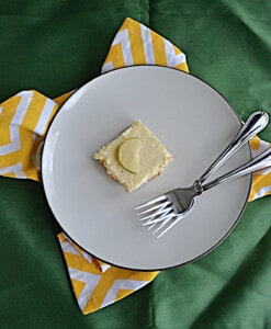 A plate with a margarita cheesecake bar with a lime on it and two forks.