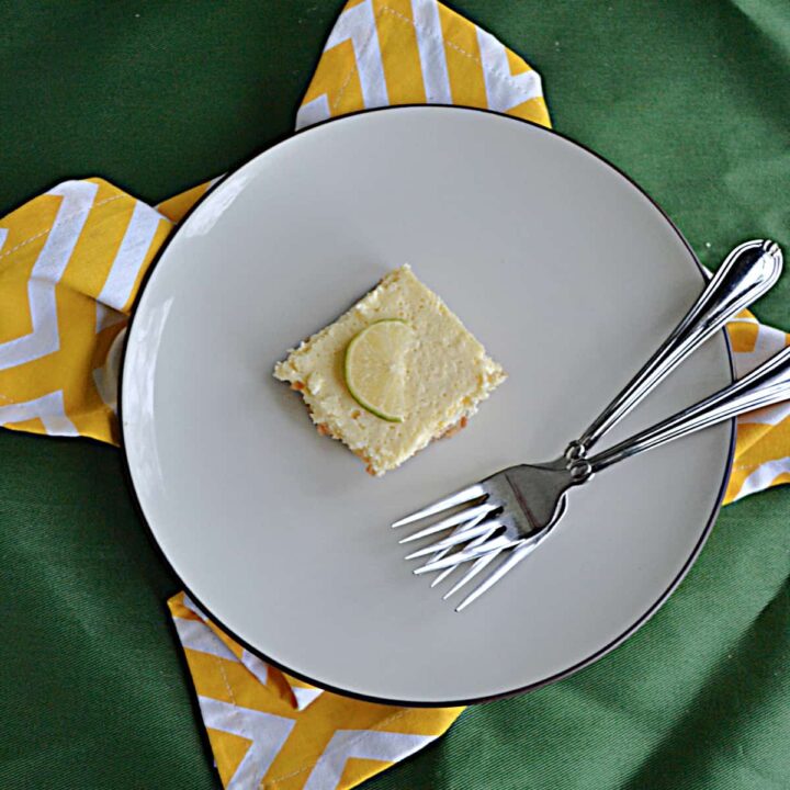 A plate with a margarita cheesecake bar with a lime on it and two forks.
