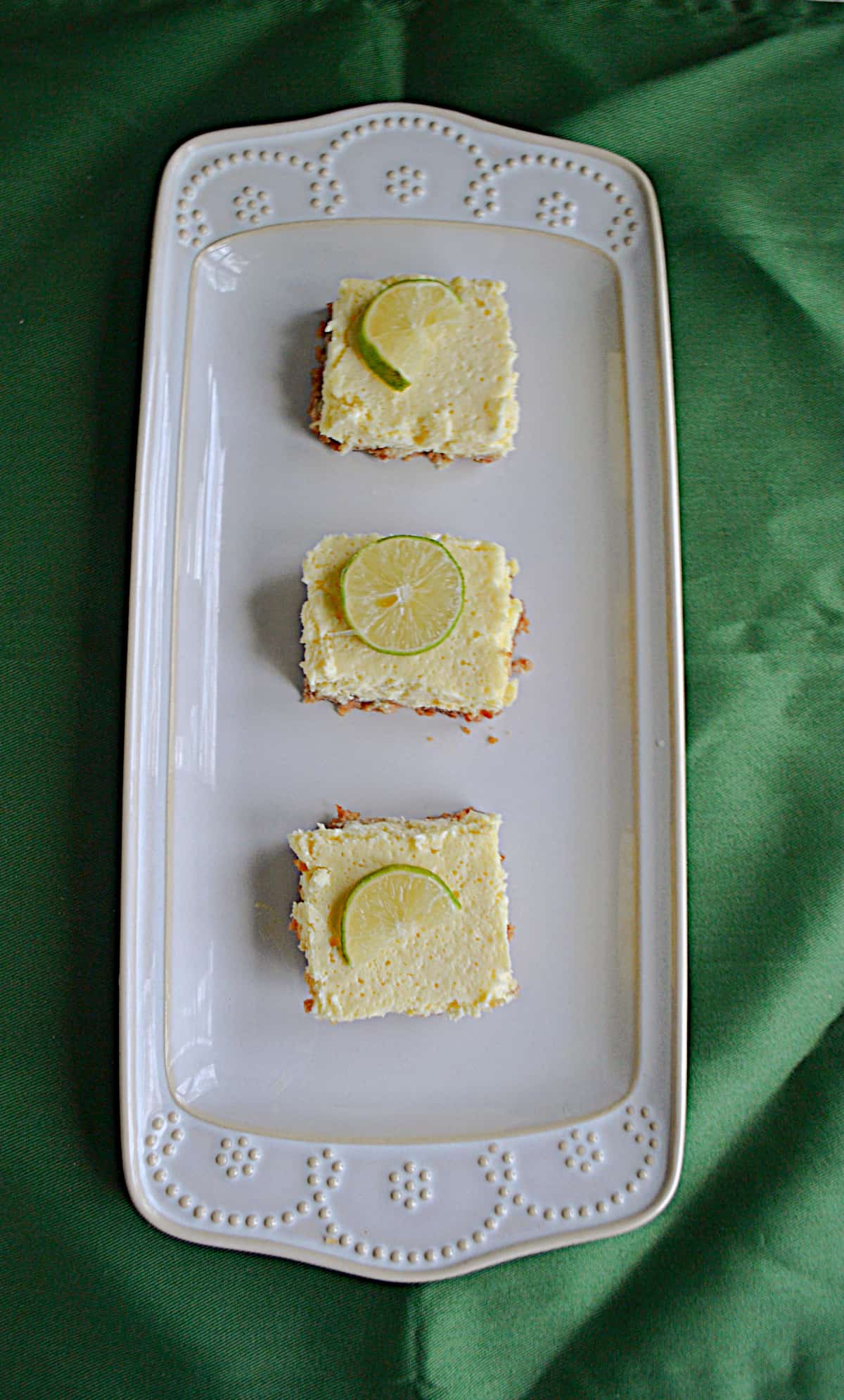A platter with three margarita cheesecake bars topped with limes.