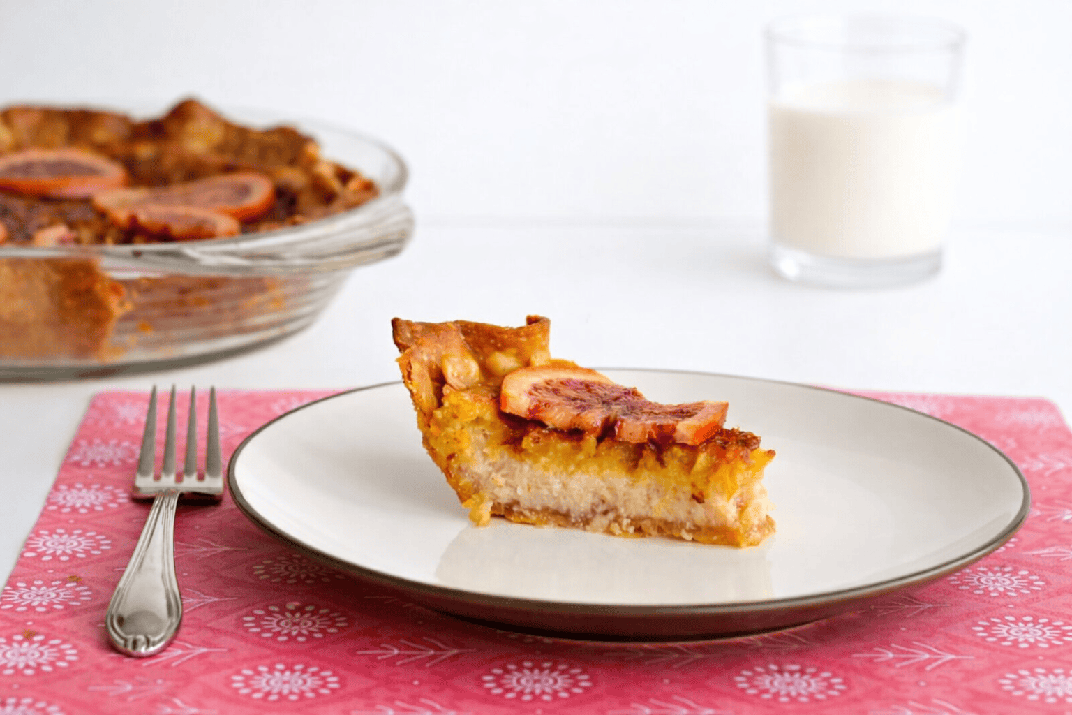 A close up of the side of a slice of orange chess pie with the whole pie in the background.