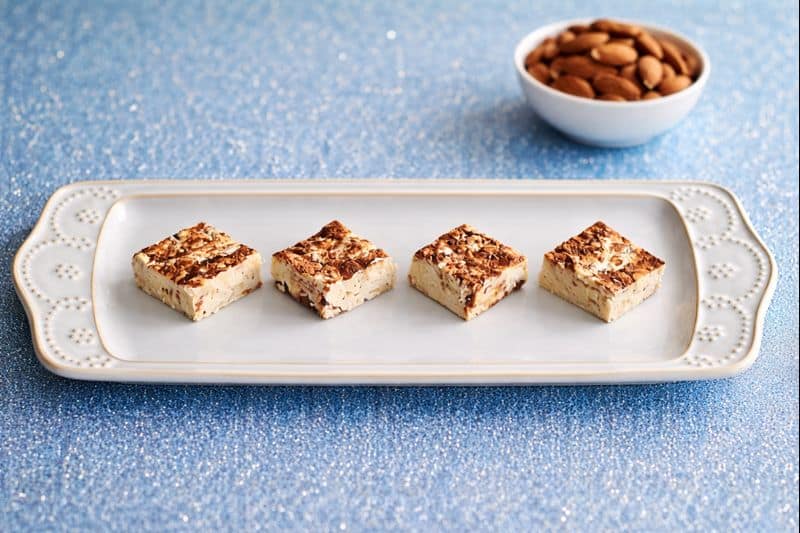 A plate with pieces of nougat on it and a bowl of chocolate chips in the background.