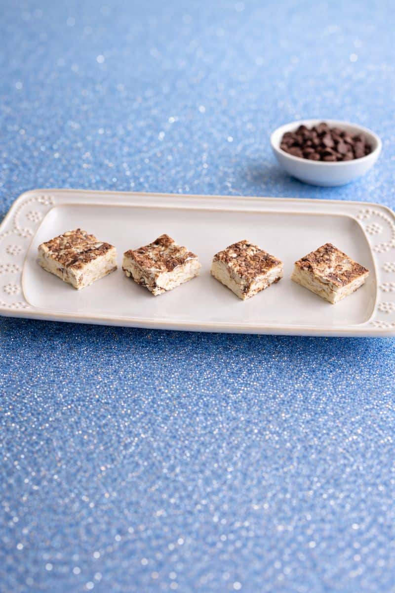 A plate with squares of nougat on it and a bowl of chocolate chips in the background.