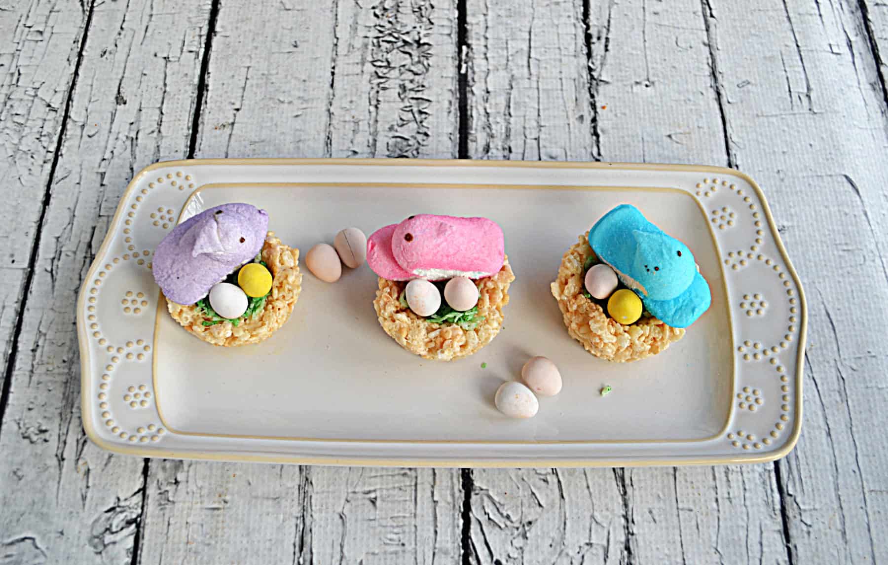 A platter with 3 bird's nests with candy eggs and Peeps on top.
