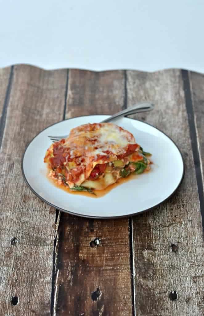 A plate with a large slice of lasagna on it along with a fork. 