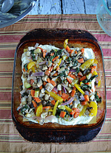 A pan with lasagna noodles topped off with ricotta cheese and sauteed vegetables