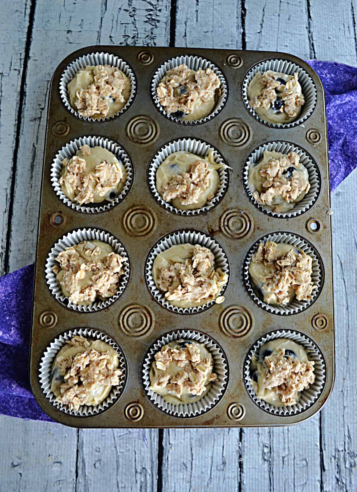A muffin tin filled with blueberry muffin batter.