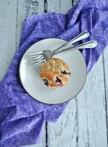 A plate with a muffin and 2 forks on it.