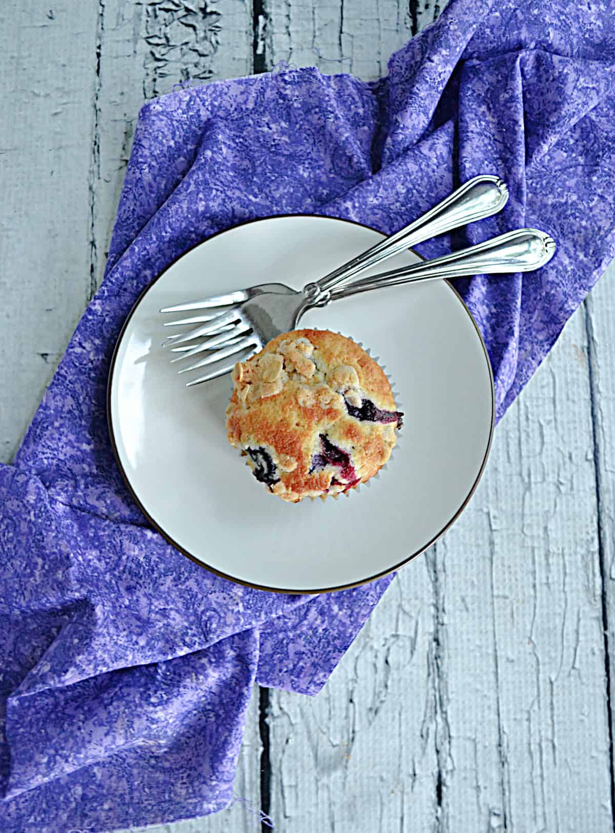 A plate with a muffin and 2 forks on it.