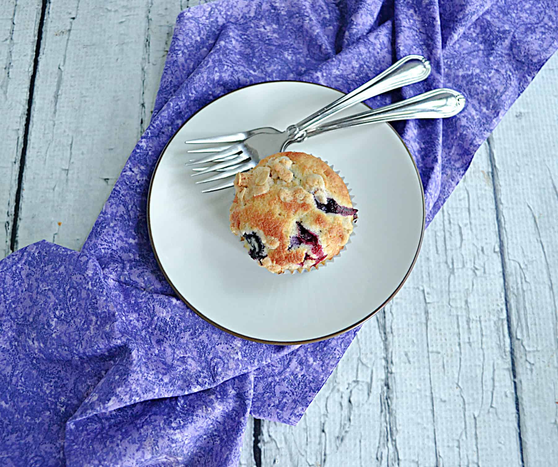 A purple background with a plate with a muffin and 2 forks on it.