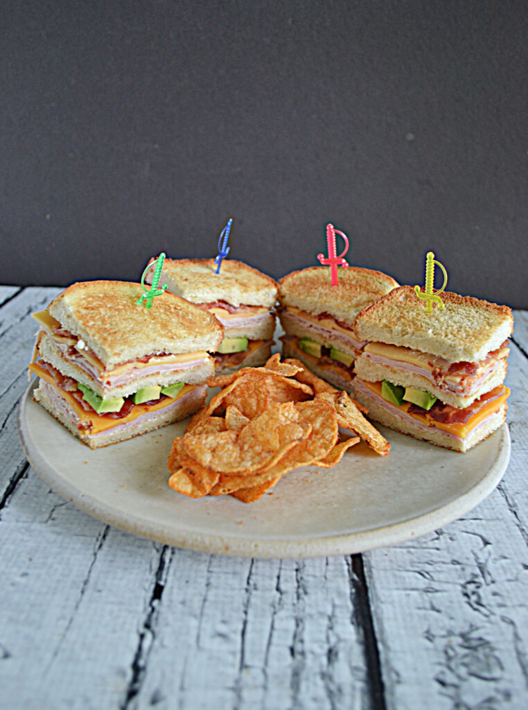 A front view of a plate with four stacks of sandwich quarters and a pile of chips in the middle. 