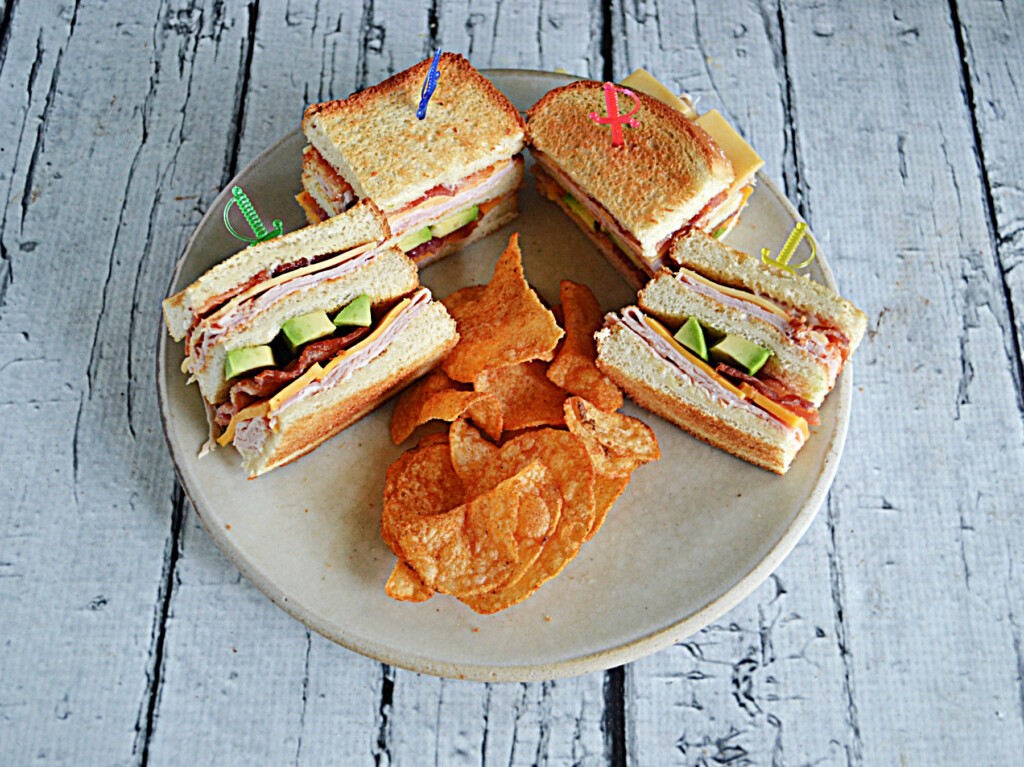 Four club sandwich pieces on a plate with a handful of chips.