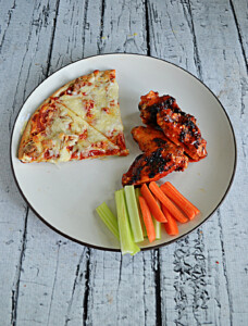 A plate with 2 slices of pizza, three grilled wings in hot sauce, and a handful of carrot and celery sticks.