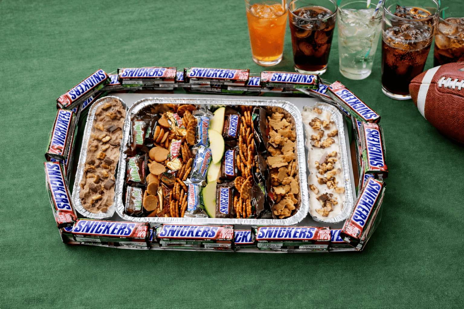 A snack stadium with giant Snickers bars, glasses of soda, and a football.