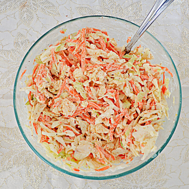 A glass bowl of cole slaw with a spoon in it.
