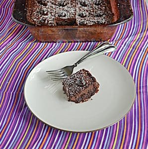 A plate with a chocolate cranberry brownie and two forks on it with the pan of brownies behind it.