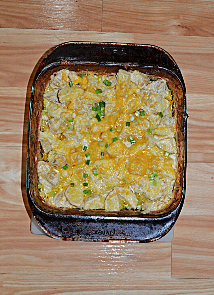 A baking dish filled with potatoes in a Ranch and cheese sauce topped with cheddar cheese and scallions. 